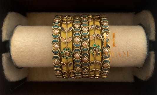 Golden silk thread bangles with green accents displayed on a wooden stand.