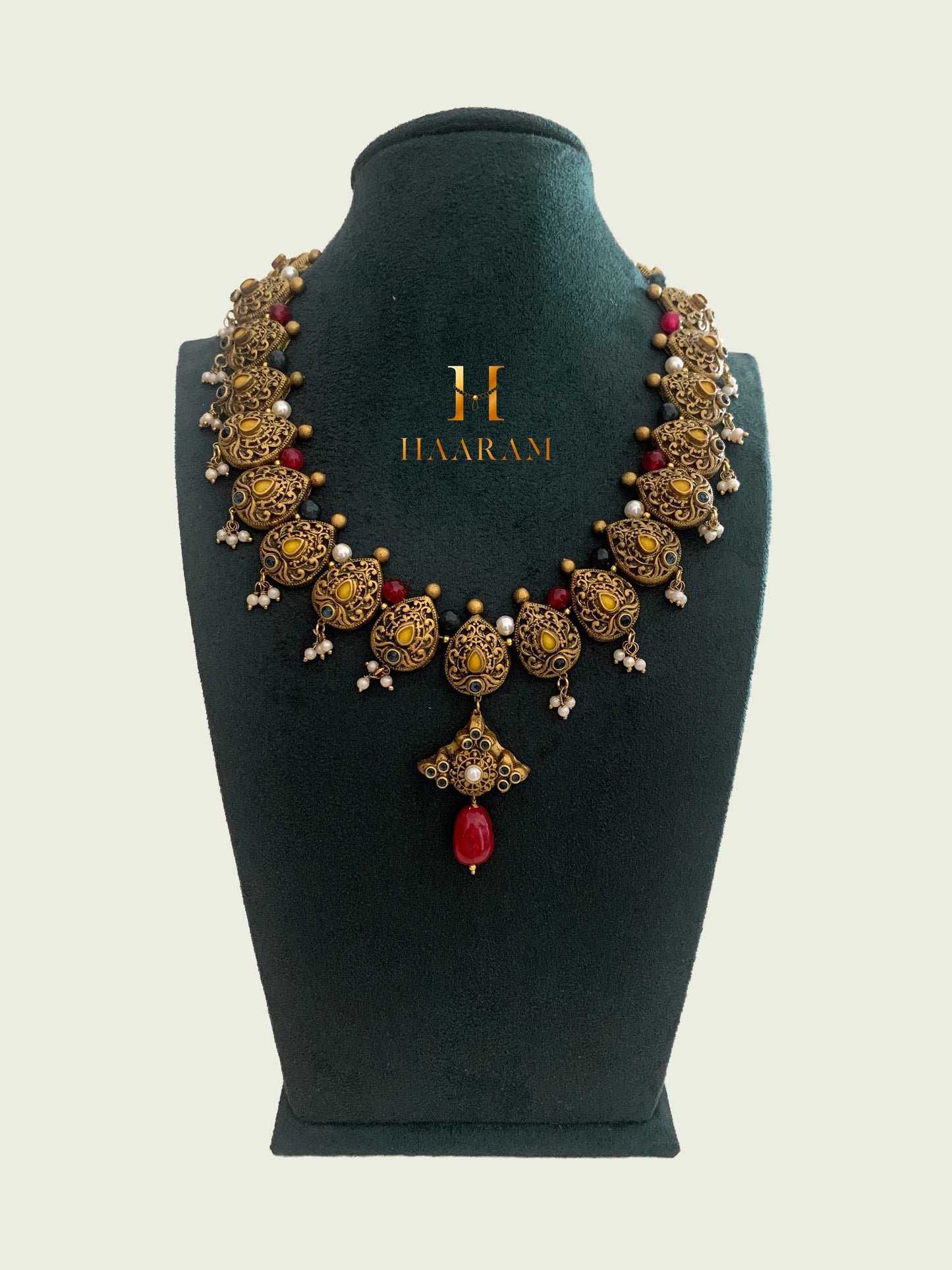 Exquisite antique Terracotta necklace set from Haarambyyashh, featuring intricate floral motifs, pearl accents, and a prominent red pendant, displayed on a jewelry stand.
