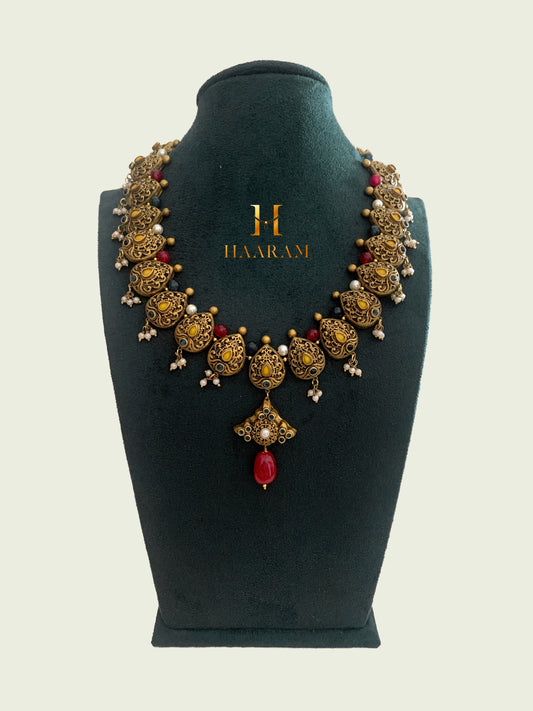 Exquisite antique Terracotta necklace set from Haarambyyashh, featuring intricate floral motifs, pearl accents, and a prominent red pendant, displayed on a jewelry stand.