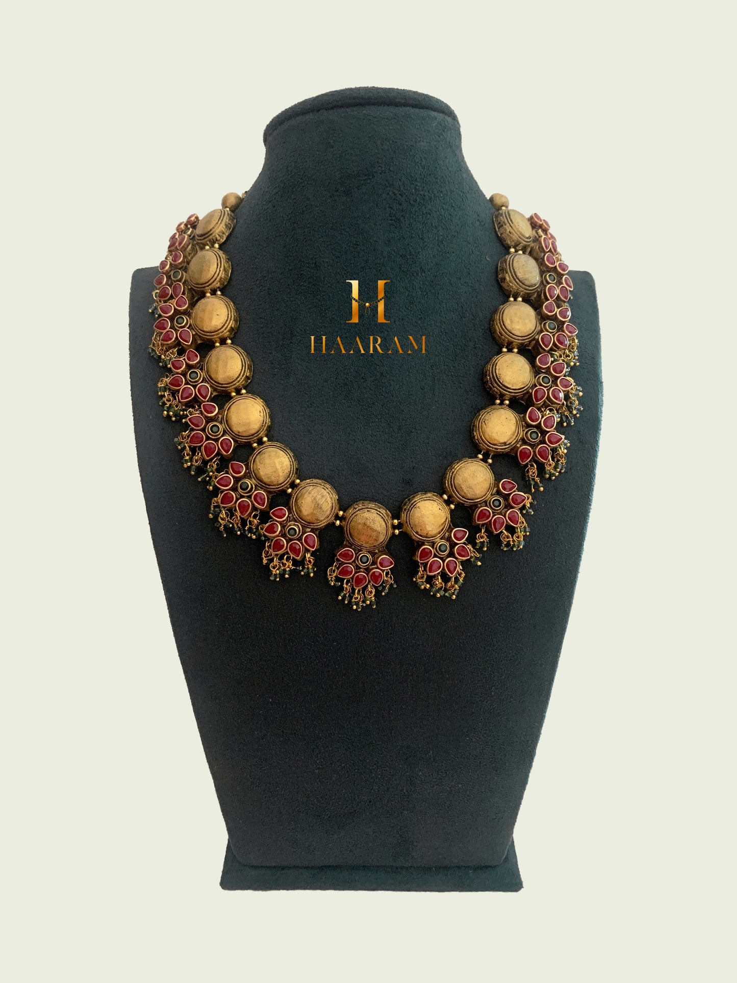 Traditional Indian Terracotta necklace from Haarambyyashh, featuring intricate red and gold design elements, displayed on a black jewelry stand