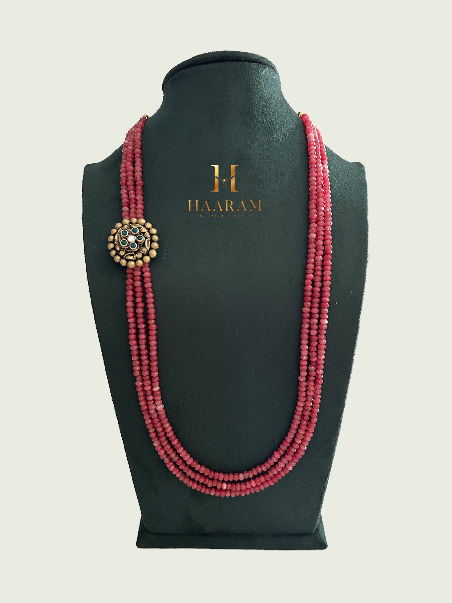 Triple-strand red beads necklace with an terracotta pendant by Haarambyyashh displayed on a jewelry stand.