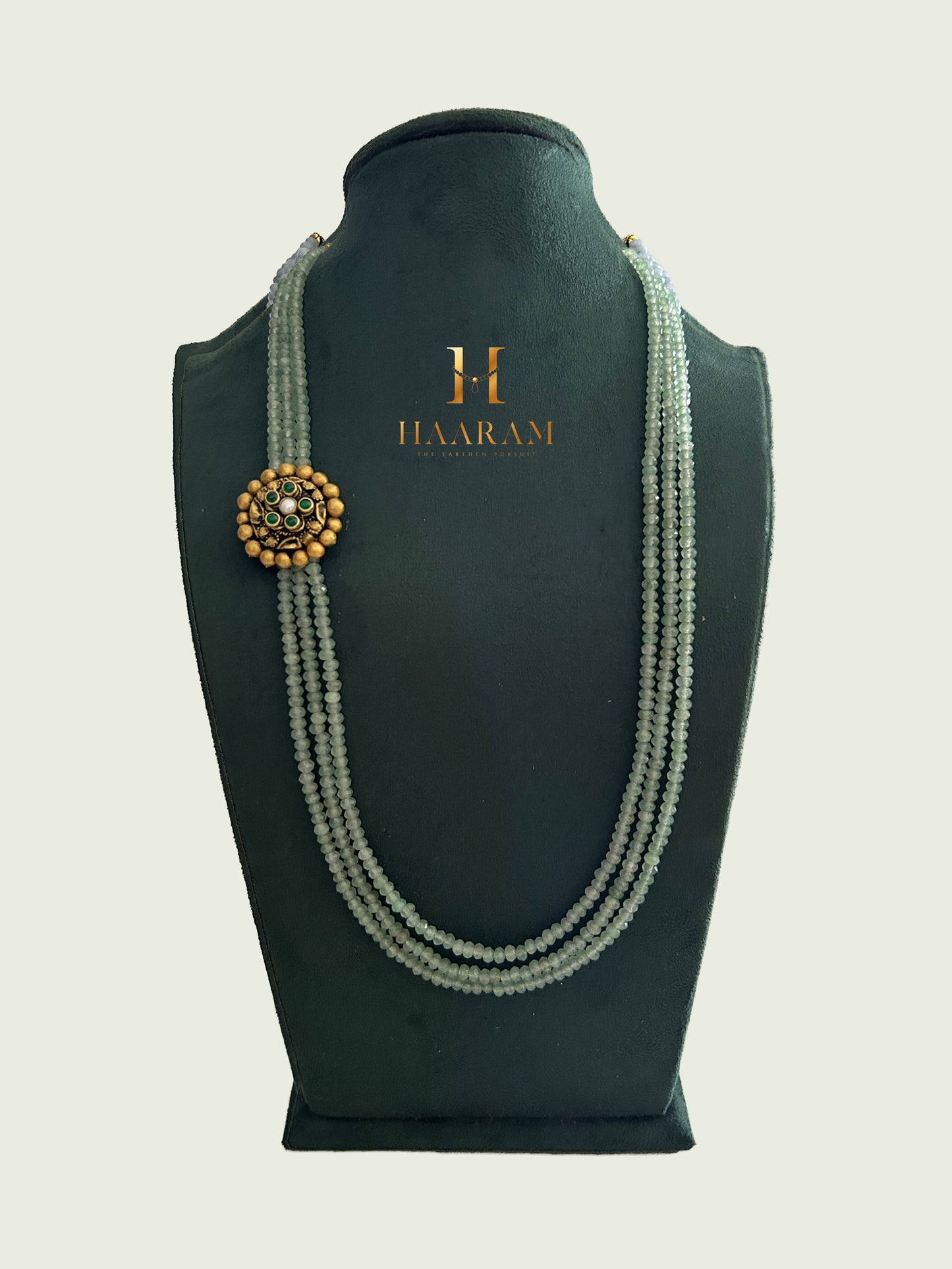 Triple-strand light green beads necklace with an terracotta pendant by Haarambyyashh displayed on a jewelry stand.
