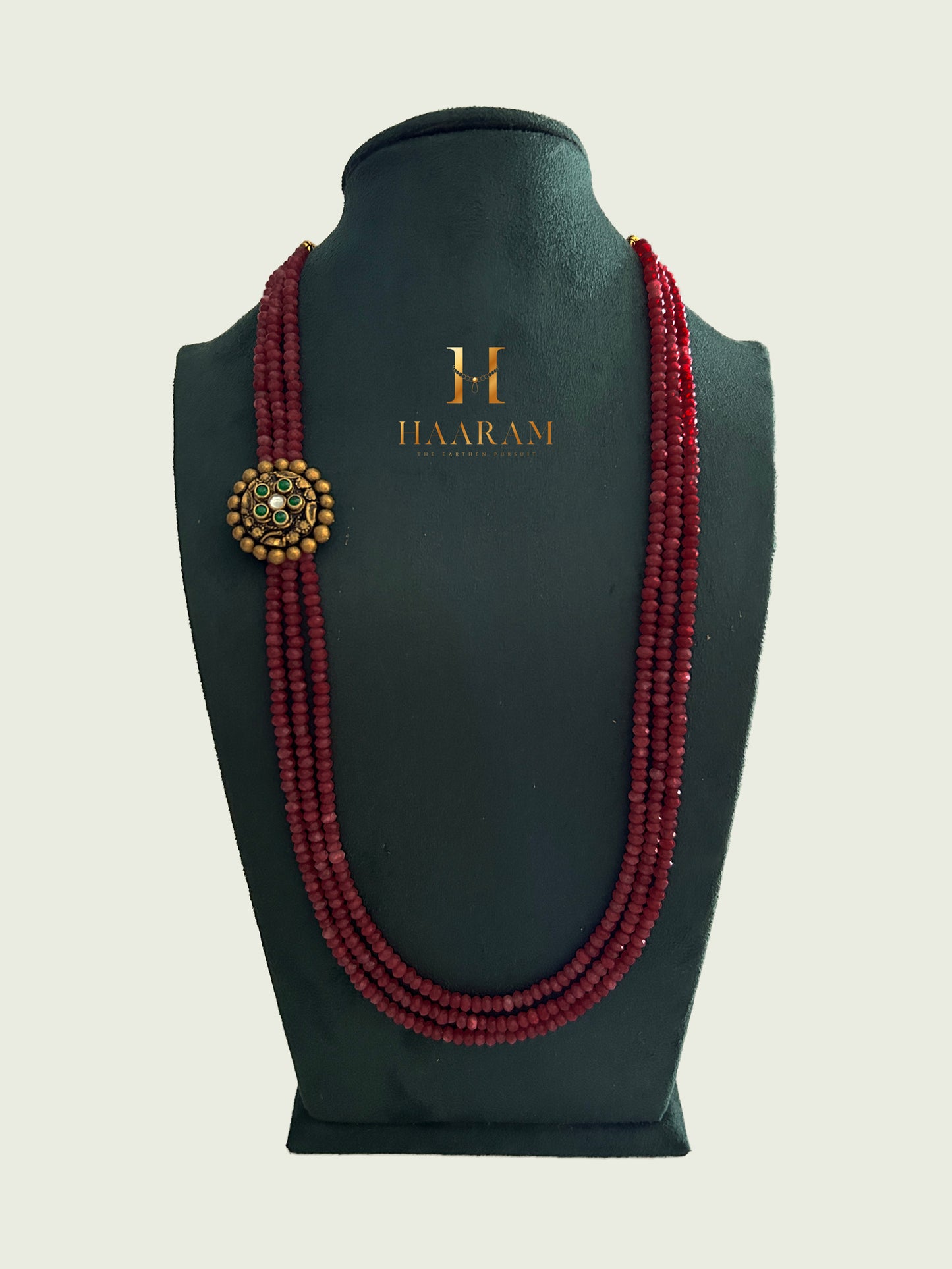 Triple-strand maroon beads necklace with an terracotta pendant by Haarambyyashh displayed on a jewelry stand.