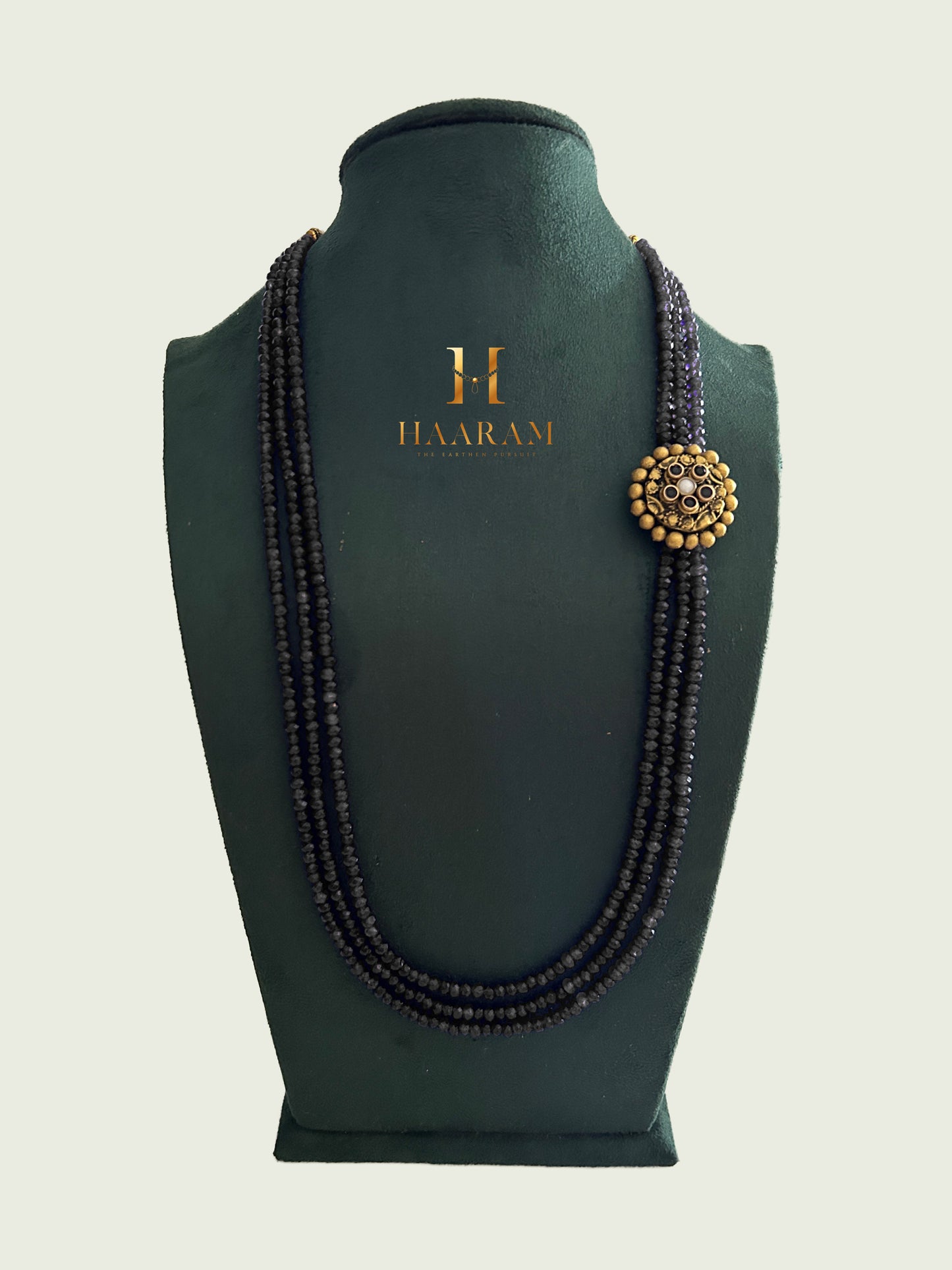 Triple-strand black beads necklace with an terracotta pendant by Haarambyyashh displayed on a jewelry stand.