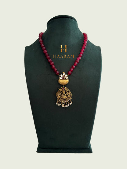 Ruby-red beaded terracotta necklace with antique gold deity pendant by Haarambyyashh.
