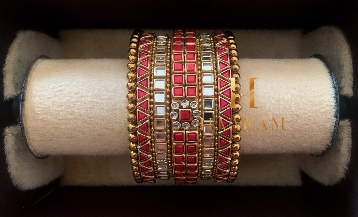 Red and gold silk thread bangles with stone accents displayed on a wooden stand.