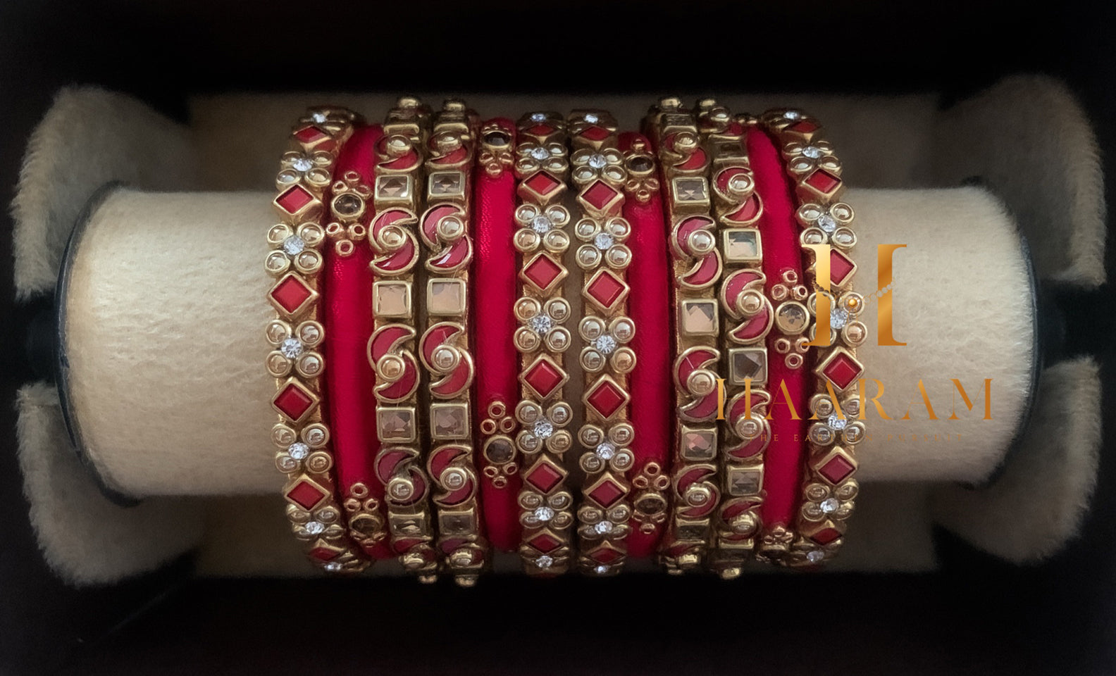 Bold red silk thread bangles with stones displayed on a wooden stand.