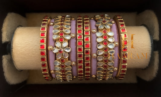 Red silk thread bangles with golden accents and shimmering stones displayed on a wooden stand.