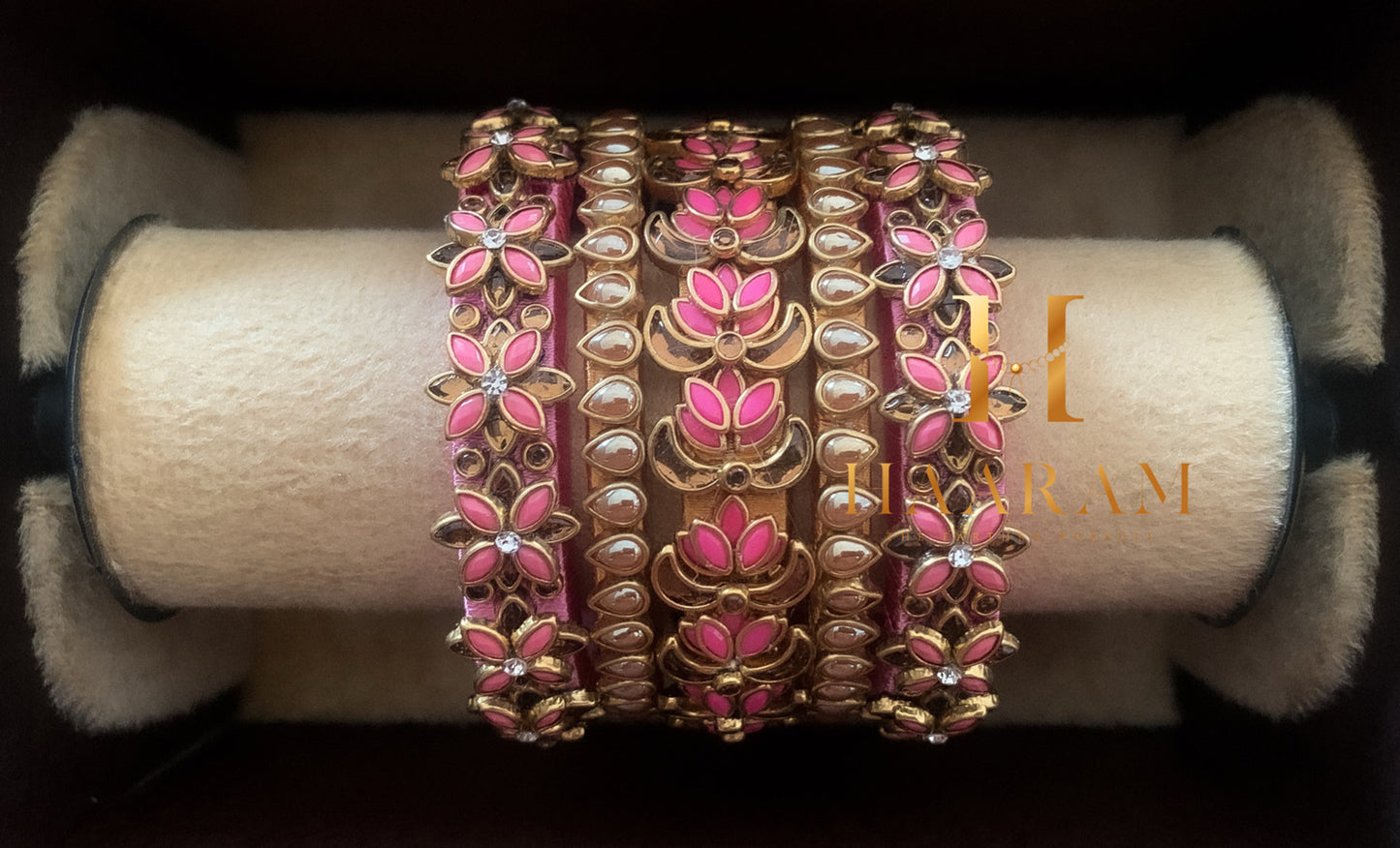 Pink silk thread bangles with stone embellishments displayed on a wooden stand.