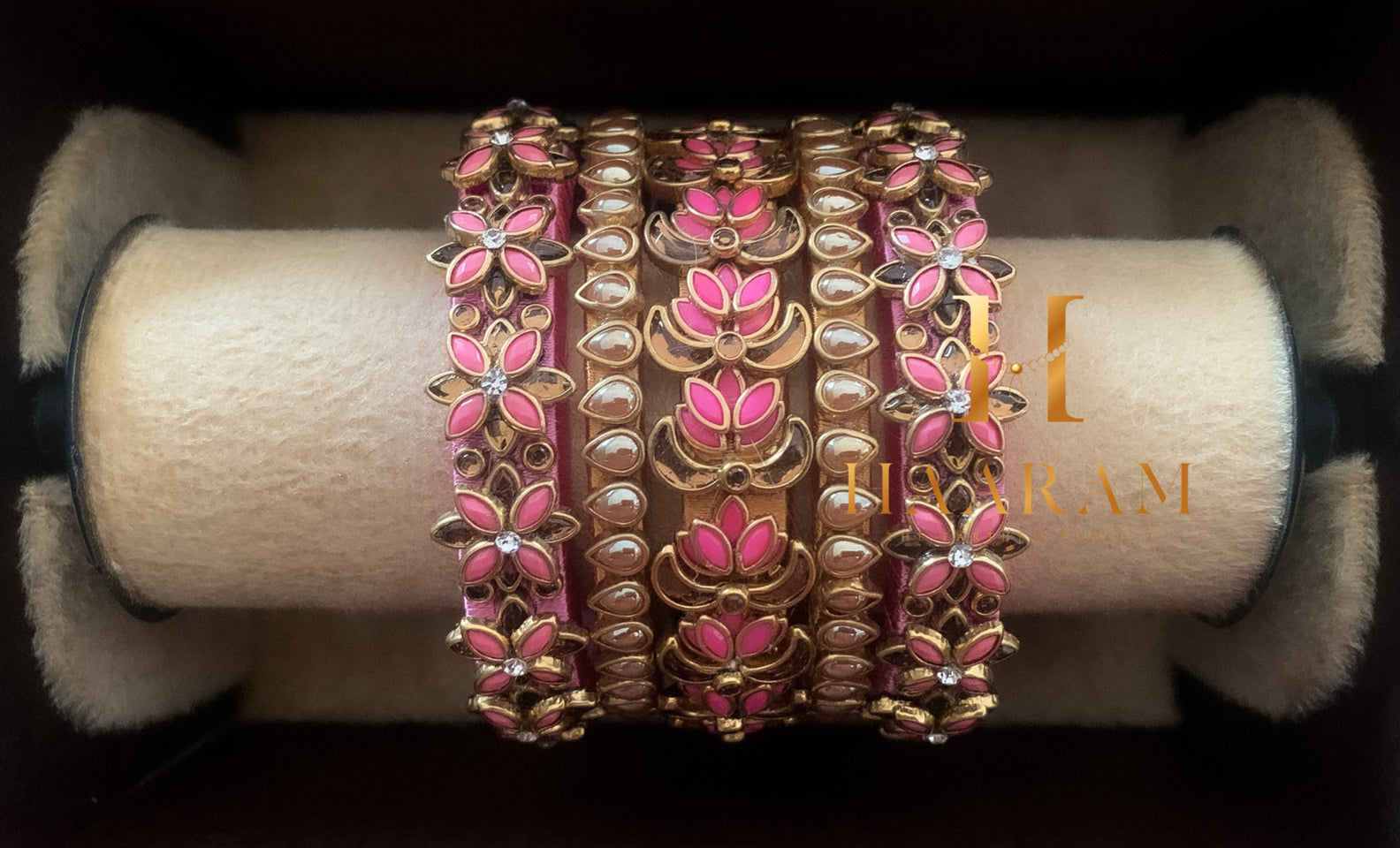 Pink silk thread bangles with stone embellishments displayed on a wooden stand.