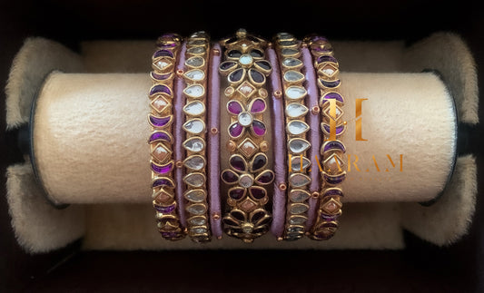 Purple and gold silk thread bangles with sparkling stones displayed on a wooden stand.