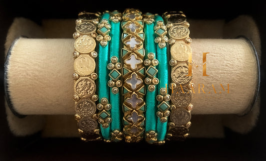 Turquoise and gold silk thread bangles with golden accents displayed on a wooden stand.