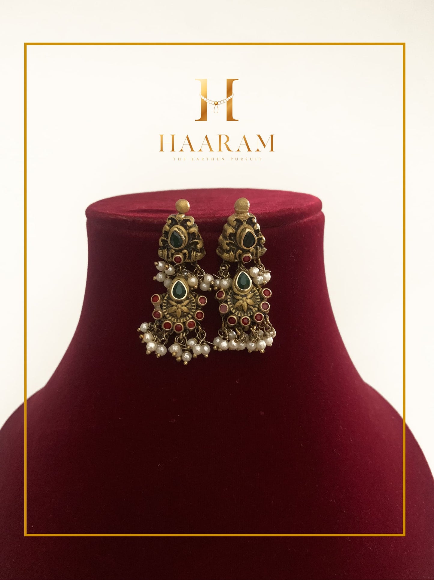 Handcrafted terracotta earrings with intricate detailing, pearls, and green and Maroon accents by Haarambyyashh, displayed on a maroon velvet stand. Perfect for ethnic and festive wear.