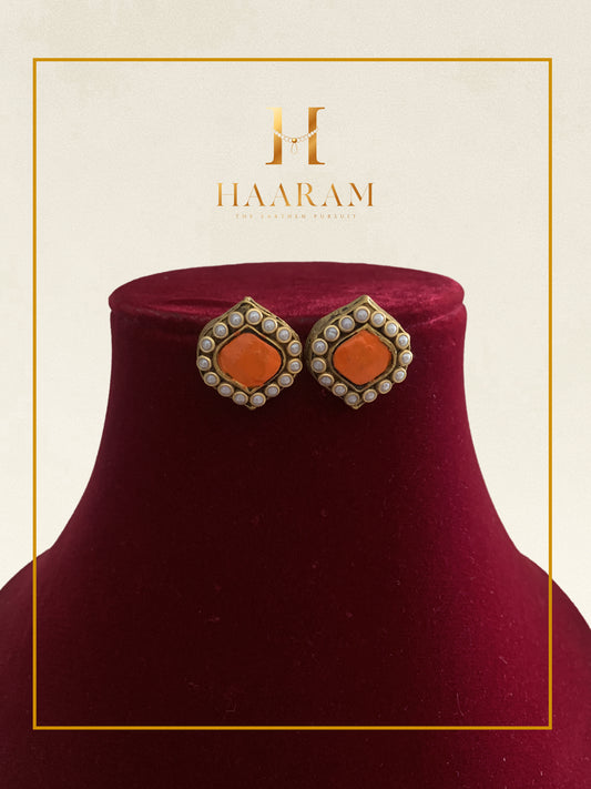 Orange stone stud earrings with kundan work displayed on a red stand.