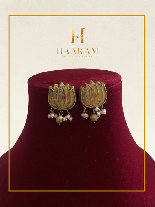 Antique gold earrings with floral motifs and pearl drops displayed on a red stand.