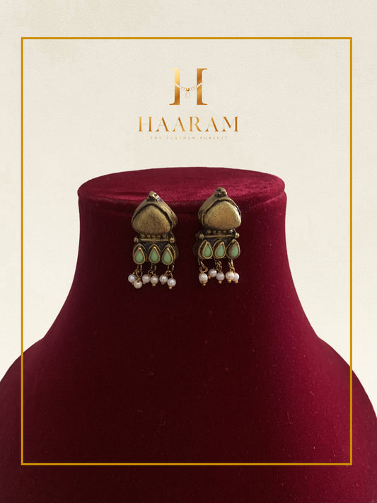 Traditional gold jhumka earrings with pearl accents displayed on a red stand.