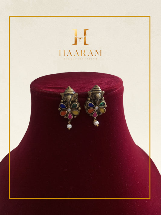 Multi-stone earrings with vibrant accents and pearl drops displayed on a red stand.