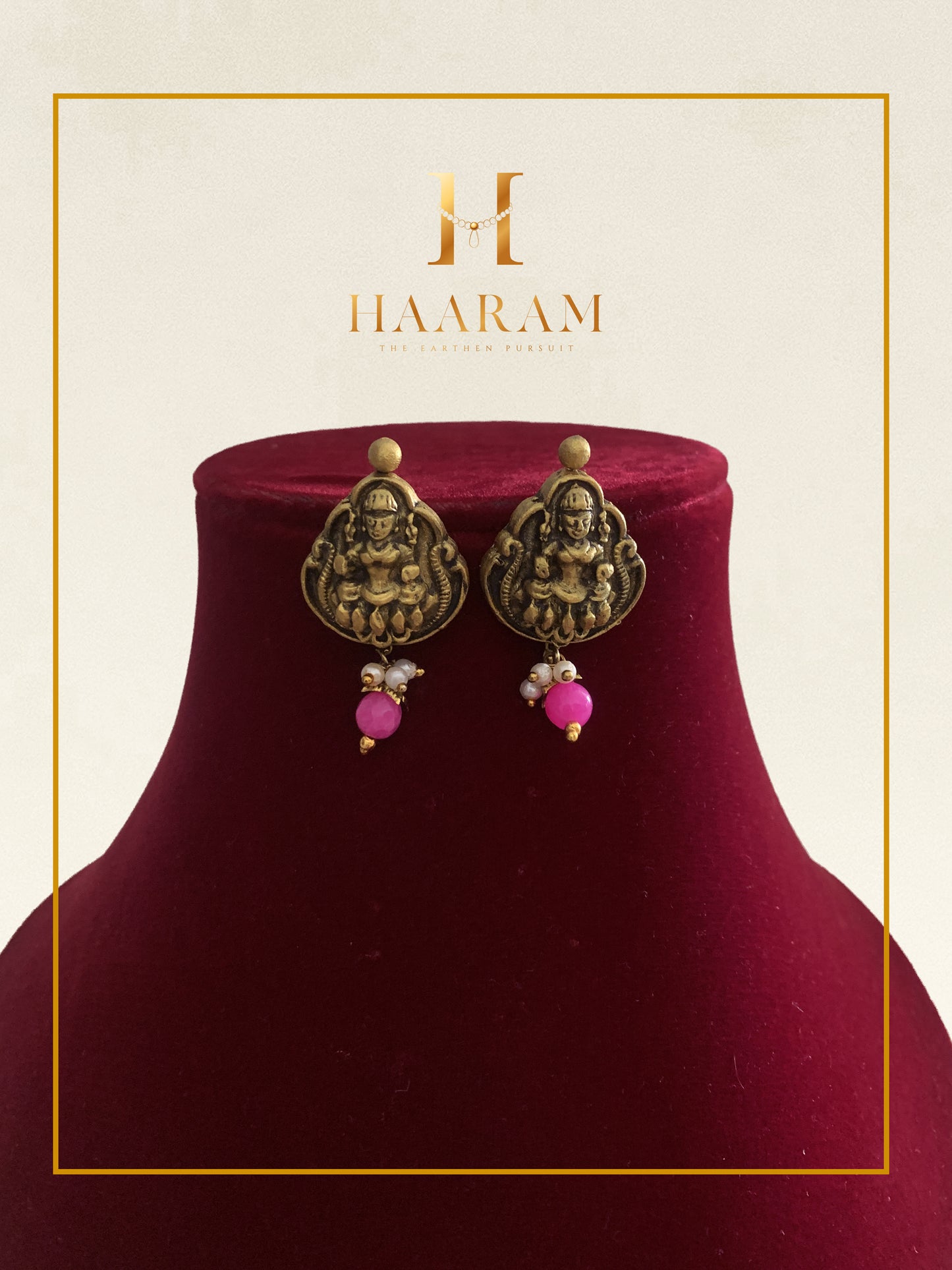 Antique-style jhumka earrings with pink bead drops displayed on a red stand.