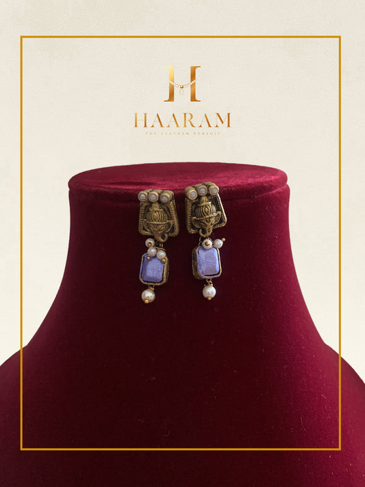 Gold earrings with blue stone accents displayed on a red stand.