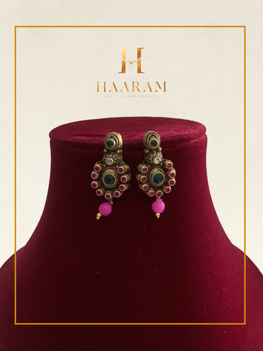 Antique-style earrings with pink bead drops and intricate kundan work displayed on a red stand.