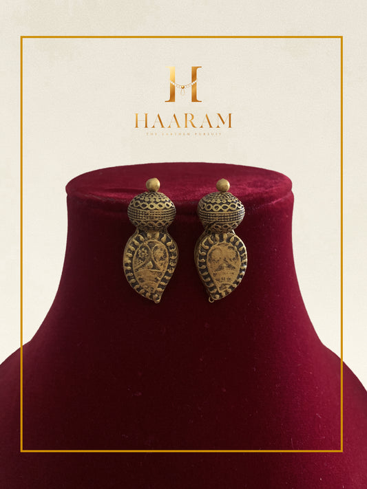 Antique gold teardrop earrings by Haarambyyashh displayed on a red stand.