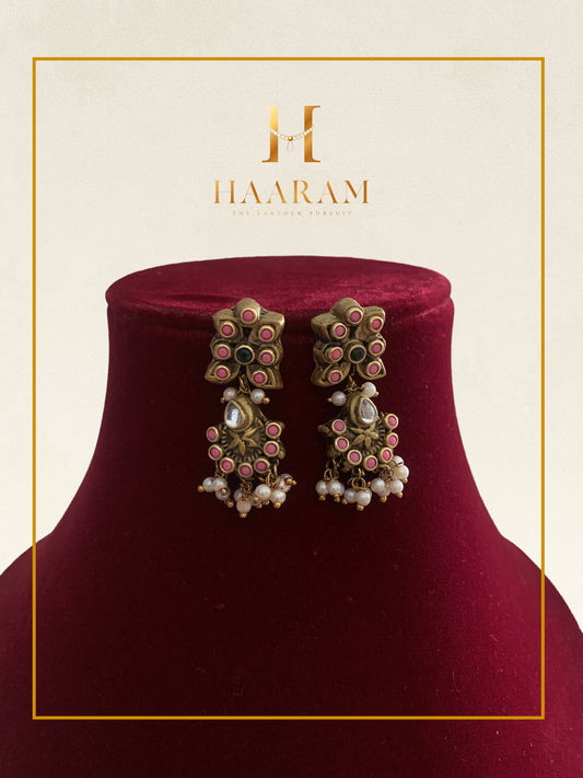 Chandelier earrings with intricate design and pearl beads displayed on a red stand.