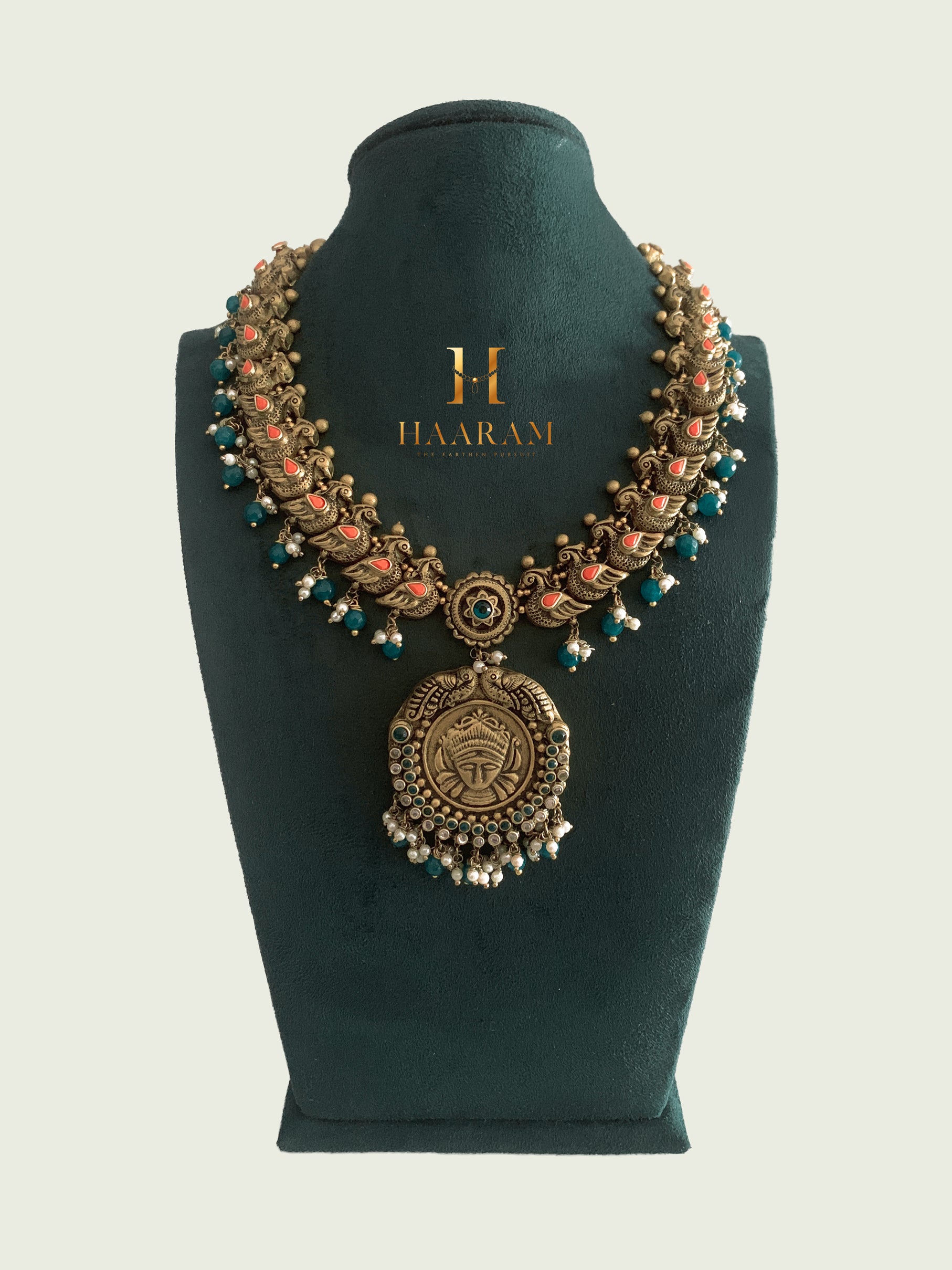 Antique terracotta necklace with teal and coral accents, featuring a large circular pendant, displayed on a black stand by Haarambyyashh