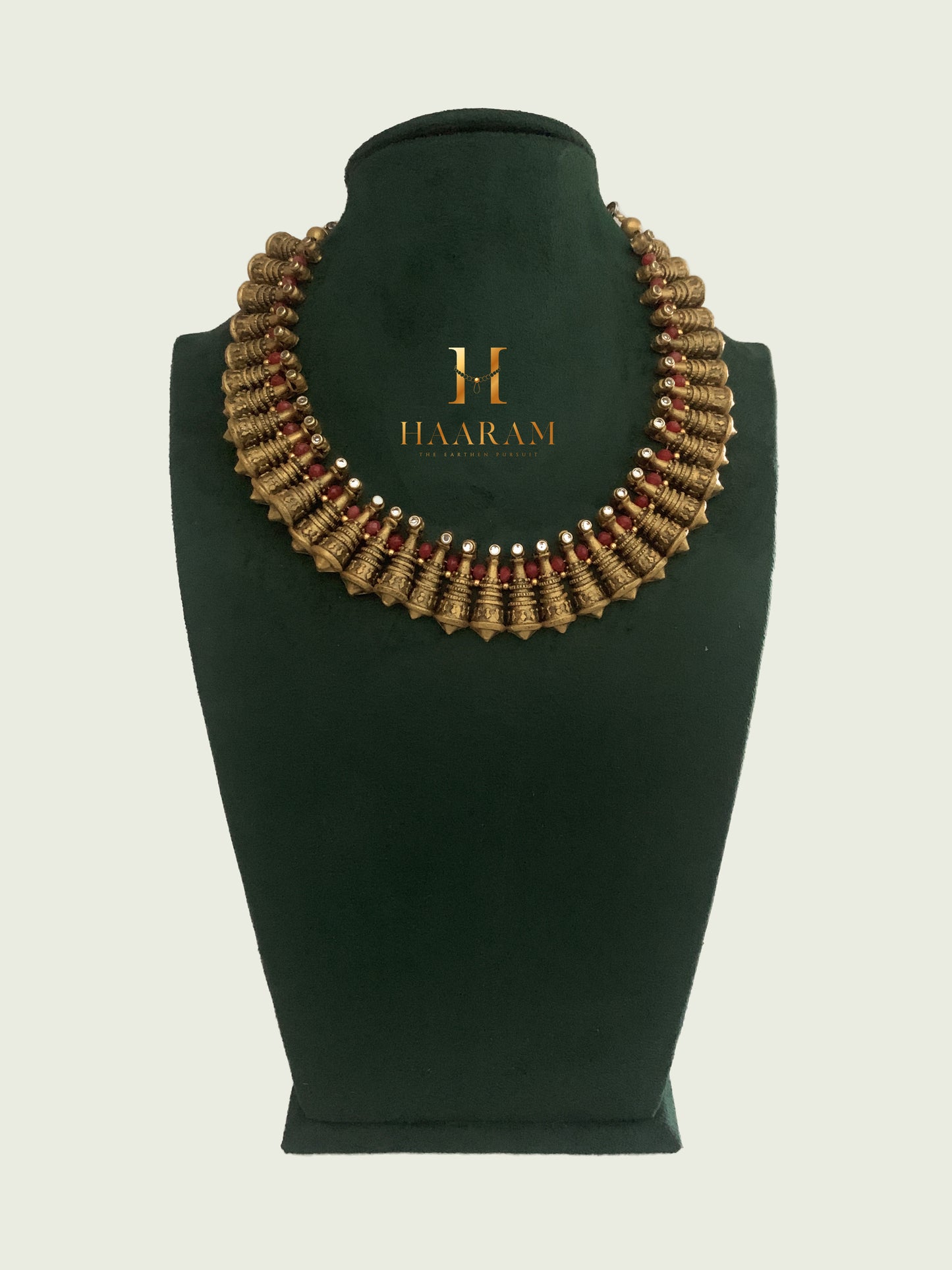 Handcrafted terracotta necklace with intricate detailing and earthy tones by Haarambyyashh, displayed on a green velvet stand. Ideal for ethnic wear.