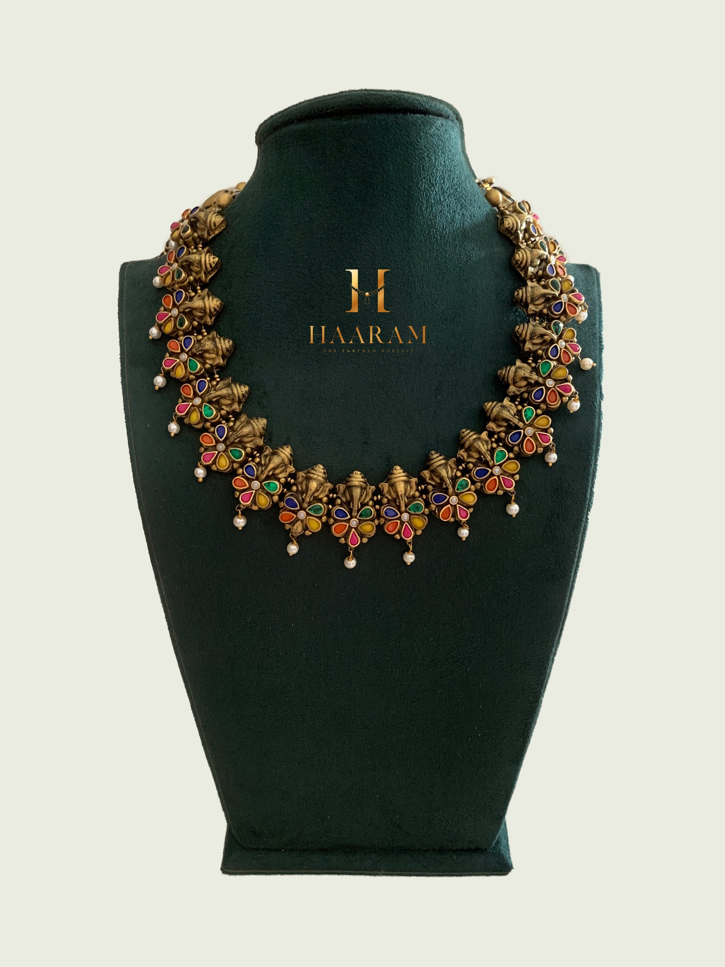 Terracotta necklace by Haarambyyashh featuring vibrant floral designs, intricate detailing, and pearl drops, displayed on a green jewelry stand.