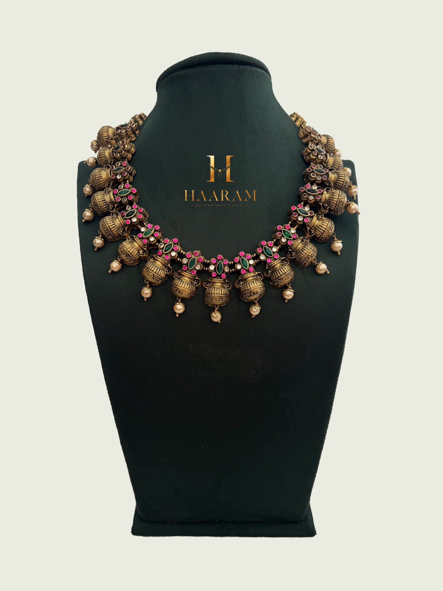 Handcrafted terracotta necklace with pink and green stones displayed on green mannequin